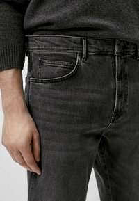 Jeans in denim nero con una vestibilità aderente, caratterizzati da cinque tasche, una texture sottile e una chiusura con bottone. Il materiale appare leggermente consumato.