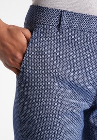 Navy patterned trousers with a textured fabric, featuring a subtle geometric design. Open pocket visible on the right side.