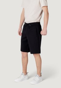Black cotton blend shorts with a drawstring waist, side pockets, and a relaxed fit. Paired with white sneakers and a light-colored t-shirt.