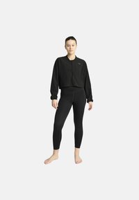 Svart kort jacka med dragkedja och långa ärmar, tillsammans med svarta leggings. Båda plaggen har en slät yta och inga påfallande mönster.