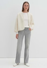 Cream-colored textured cardigan with large pockets, paired with high-waisted light gray straight-leg jeans and white sneakers. Smooth fabric.