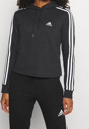 Zwarte Adidas hoodie en bijpassende trainingsbroek met witte strepen op de mouwen en benen, Adidas-logo's op de borst en dij.