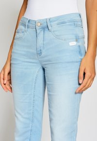 Světle modré džíny s úzkým střihem, s předním zapínáním na knoflík, pěti kapsami a jemným vyblednutím na látce.