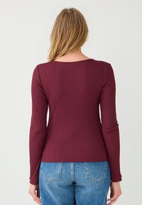 Langärmliges Oberteil aus burgunderfarbenem Rippstoff mit einem runden Rückenausschnitt und einem figurbetonten Design, kombiniert mit hoch taillierten blauen Denim-Jeans.
