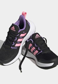 Scarpe sportive nere con accenti rosa e viola, tomaia in rete, chiusura con lacci e suola bianca; presenta un evidente design a tre strisce.