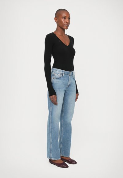 Un body de manga larga negro combinado con unos vaqueros de pierna ancha de color azul claro y unos zapatos planos granates. Los vaqueros tienen un diseño clásico de cinco bolsillos.