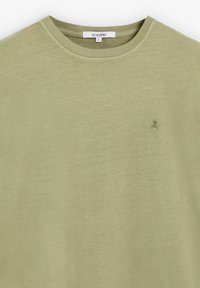 Camiseta verde olivo hecha de tela suave con escote redondo. Presenta un pequeño logo de calavera bordado en el lado izquierdo del pecho.