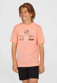 Camiseta de manga corta en color rosa pastel con un diseño gráfico y un logo en negro. Combinada con pantalones cortos oscuros, exhibida sobre un fondo neutro.