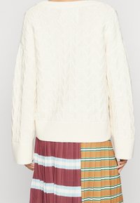 Pull en tricot blanc avec des motifs triangulaires texturés, manches larges et un ourlet côtelé. Assorti à une jupe plissée multicolore.