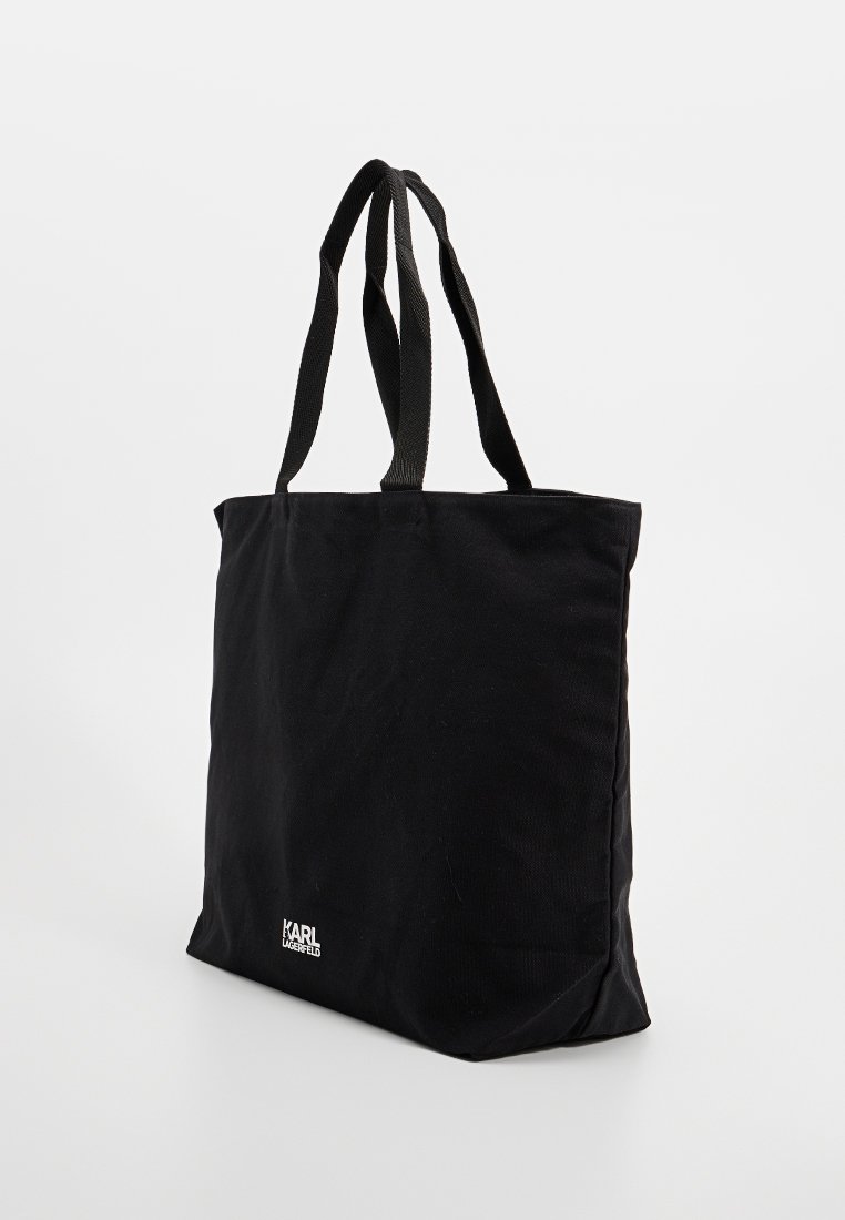 Schwarze Tote-Tasche mit doppelten Schultergurten und kleinem weißen "KARL LAGERFELD" Logo in der unteren Ecke, vor einem weißen Hintergrund stehend.