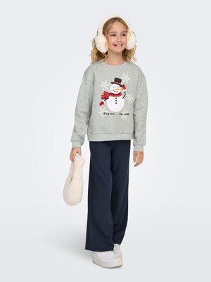 Sweat-shirt gris avec graphisme de bonhomme de neige et texte, associé à un pantalon large marine. Le modèle porte des baskets blanches et des cache-oreilles en fourrure.
