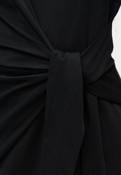 Μαύρο ύφασμα δεμένο με έναν απλό κόμπο με συγκεντρωμένες πτυχές, που δείχνει την υφή και την πτώση του υλικού.