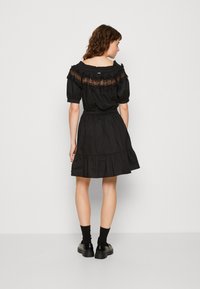 Abito nero off-the-shoulder con maniche a palloncino, dettagli in pizzo sul colletto, vita elastica e gonna a strati. Indossato con scarpe nere e calzini.