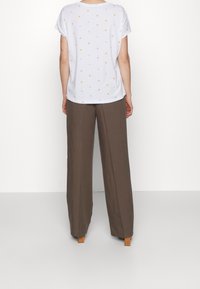 Vit kortärmad topp med prickigt mönster i pastellfärger, ihopparad med lösa bruna byxor. Enkel, avslappnad passform.