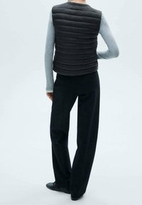 Czarna kamizelka puchowa z poziomym pikowaniem, zestawiona z jasnoszarym topem z długim rękawem i czarnymi szerokimi spodniami. Estetyka minimalistyczna.