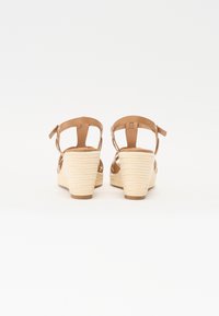 Sandales compensées avec des sangles en simili cuir marron et un talon en corde beige texturée. Comprend des sangles de cheville réglables et un design à talon fermé.