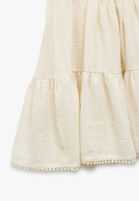 Cremefarvet, lagdelt nederdel i tekstureret stof, med flæsekanter og delikat pom-pom-b trim nederst. Blød og svævende design.