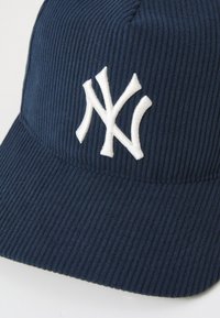 Navy corduroy cap featuring a white embroidered logo. Structured design with a textured surface and a curved, stitched brim.