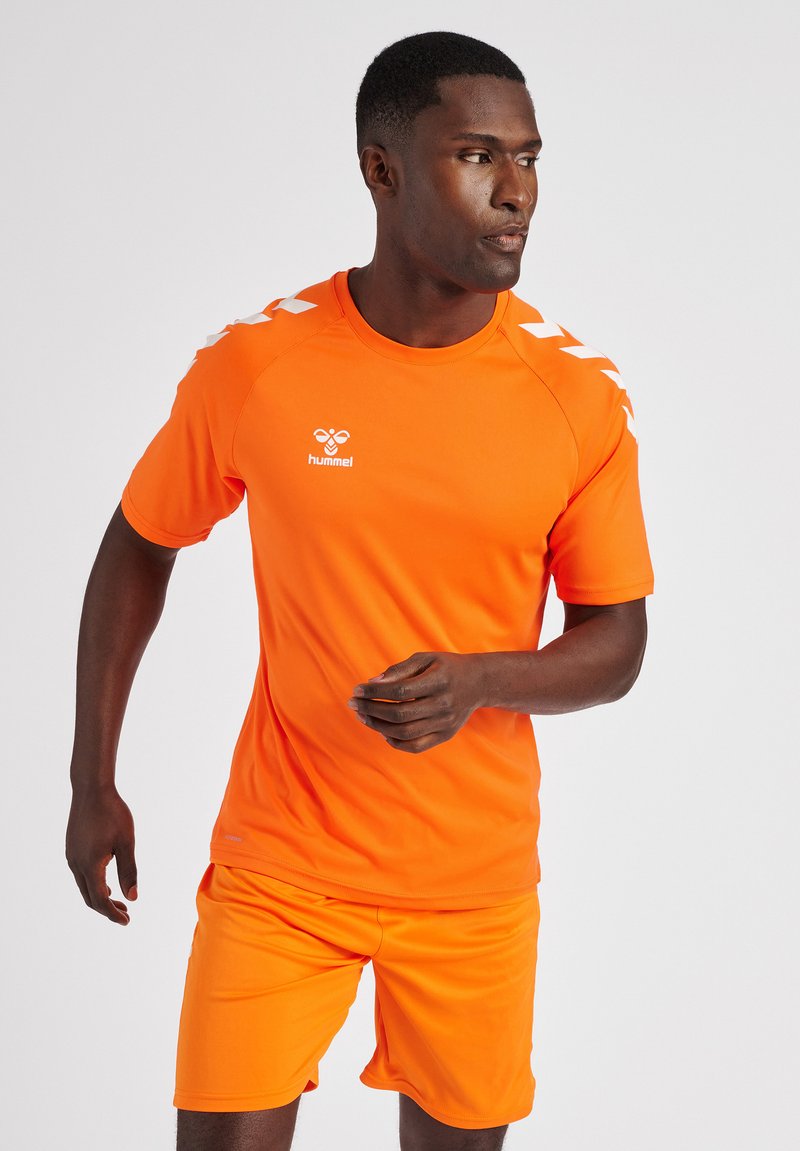 T-shirt et shorts de sport orange en tissu lisse et léger. Présente un logo blanc et des accents en chevron sur les épaules.