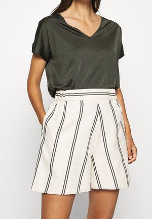 Woman wearing dark green V-neck short-sleeve top tucked into high-waisted white shorts with vertical black stripes and elastic waistband.