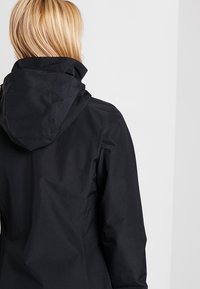 Svart vattentät jacka med hög krage och justerbar huva, med en slät yta och minimalistisk design. Bakvy visas.