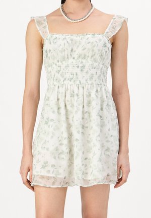 Robe légère sans manches à motif floral avec bretelles volantées et taille froncée, portée avec un collier de perles et une chaîne en argent.