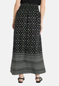 Falda maxi negra con cintura fruncida, que presenta un patrón geométrico blanco y una banda decorativa en el dobladillo. Tela ligera y fluida.