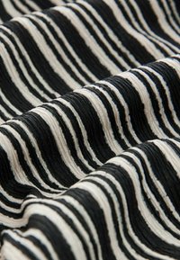 Tissu avec des rayures alternées noires et crème, présentant une surface texturée et côtelée qui crée de la profondeur et du contraste dans le motif.