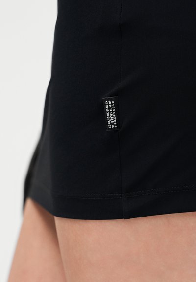 Fekete rövidnadrág sima anyagból, oldalán kis címkével, melyen számadatok láthatók. Az alja varrott, tiszta befejezést biztosítva.