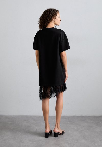 Fekete, túlméretezett pólóruha rövid ujjakkal, csipkés díszítéssel az alján. A ruha sima textúrával és laza szabással rendelkezik.