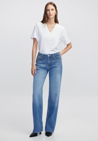Witte v-hals top met korte mouwen, gecombineerd met lichtblauwe wijde jeans met een kraalpatroon en zilverdraaddetails.