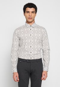 Witte overhemd met knopen en een geometrisch patroon in blauw, groen en bordeauxrood. Heeft een klassieke kraag en manchetten. Draagt bijpassende donkergrijze broek.