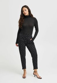 Zwarte lange mouwen turtleneck en zwarte broek met witte hartpatronen, met een relaxte pasvorm en zakken, gecombineerd met zwarte haksandalen.