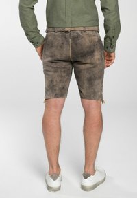 Braune Lederhorts mit strukturiertem Aussehen, ausgestattet mit Schnürdetails an den Seiten und gestickten Akzenten. Tragen mit weißen Sneakers.