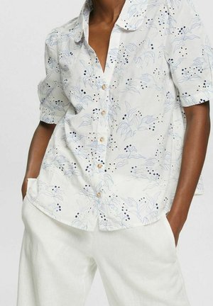 Person wearing a white short-sleeve button-up shirt with a delicate blue and black leaf and berry pattern, paired with white pants.