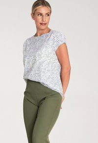 Biały top z krótkim rękawem z czarnym, ręcznie napisanym wzorem, włożony w oliwkowe, dopasowane spodnie. Gładki materiał; luźny krój.