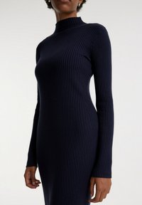 Robe en tricot côtelé marine avec un col haut et des manches longues, présentant une silhouette ajustée et un matériau texturé. Fini lisse.