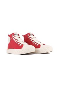 Sneakers alte rosse con suole in gomma bianca, tomaia in tela, lacci piatti e una toppa circolare laterale; presentano una suola testurizzata e accenti a contrasto.