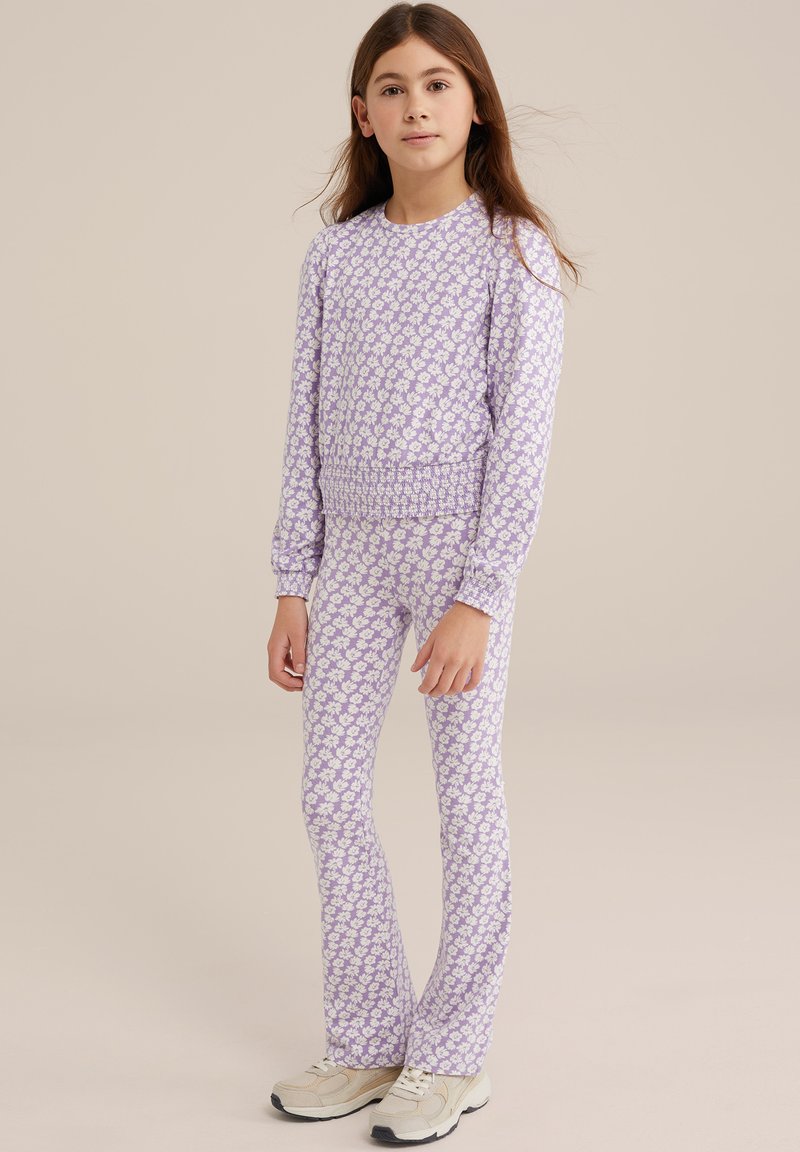 Lila pyjamaset med blommönster, elastisk midja och långa ärmar. Kombineras med krämfärgade sneakers. Slät tygkvalitet.