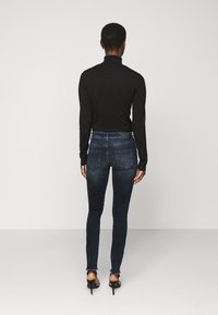 Zwarte coltrui gecombineerd met donkerblauwe, nauwsluitende jeans met een licht rafelige zoom en twee achterzakken. Gecombineerd met zwarte hoge hakken.