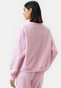 Różowy sweter, miękka tkanina, luźny krój, ściągacze przy mankietach i u dołu, oraz okrągły dekolt. Widok z tyłu, o gładkiej fakturze i bez zdobień.