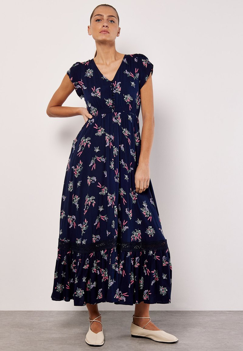 Vestido floral marino con escote en V, mangas cortas y un dobladillo en capas, con patrones en rosa y verde y un detalle de encaje.