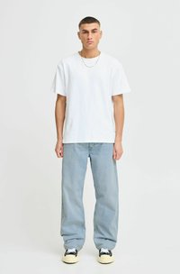 Camiseta blanca de algodón, de mangas cortas, ajuste relajado, combinada con jeans de denim azul claro, con un ajuste ligeramente holgado, llevados con zapatillas negras y crema.