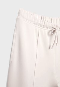 Helle beige Jogginghosen aus weichem Stoff, mit elastischem Bund, Kordelzug und Seitentaschen. Glatte, untexturierte Oberfläche.