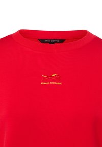 Czerwona bawełniana koszulka z prążkowanym kołnierzem i małym haftowanym logo w żółto-czerwonym wzorze na piersi. Miękka w dotyku, o prostym kroju.