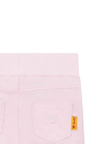 Pantalon en coton rose clair avec une texture douce, comportant deux poches arrière, un logo d'ours et une étiquette jaune sur le côté.