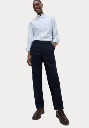 Camisa de botones a rayas de color azul claro, pantalones oscuros azules y botas de cordones marrones. El atuendo tiene un corte holgado y un estilo casual.