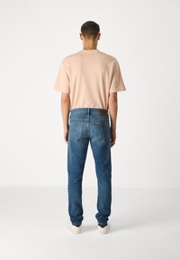 Ljusrosa t-shirt med kort ärm, blå jeans i denim med blekta partier och söm-detaljer, samt vita sneakers. Sedd bakifrån.