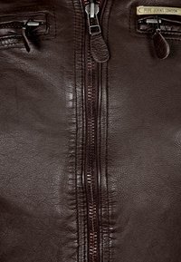 Ruskea nahkatakki, jossa on keskellä vetoketju, kaksi vetoketjullista taskua ja teksturoitu pinta, jossa on hillitty kiilto. Merkkilapussa lukee "Pepe Jeans London".