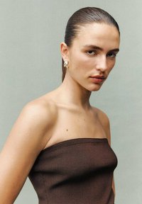 Crop top marrone senza spalline con texture a costine, modella con capelli lisci e orecchini ad anello, sfondo neutro, enfasi sui tratti del viso.